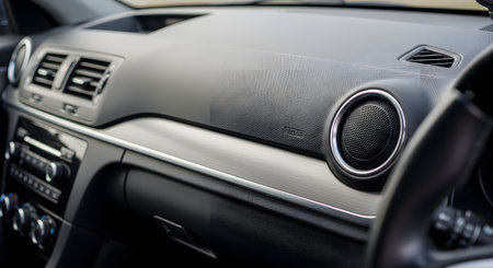 A close-up view of a modern car's interior from the passenger side. The image shows the dashboard, air vent, round speaker, brushed aluminum trim, and the 'AIRBAG' text.の素材
