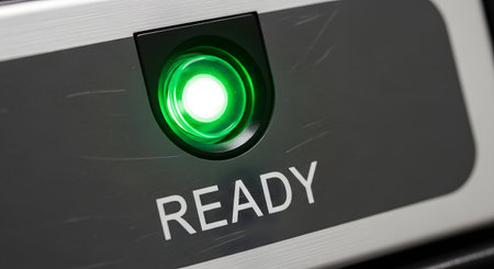 A macro close-up shot of a bright green, illuminated circular button on a brushed metal control panel with the word 'READY' printed below it. The glowing light indicates that a system is active, online, and prepared for operation.の素材