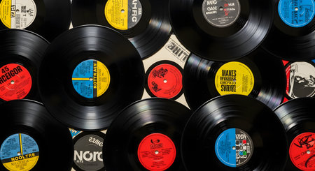 A top-down, flat lay shot of a large pile of overlapping black vinyl records. The records are LPs and 45s, with various colorful labels in the center. This image evokes nostalgia, music, and the hobby of record collecting.の素材
