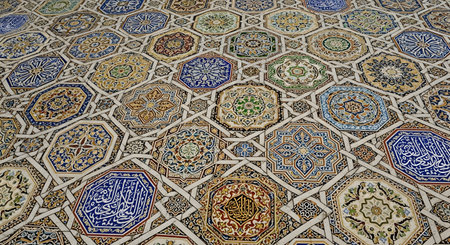 A high-angle view of an intricate and colorful mosaic tile floor, featuring complex geometric patterns, stars, and octagons. Many tiles are adorned with elegant Arabic calligraphy, showcasing traditional Islamic art, architecture, and cultural heritage.の素材