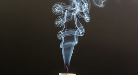 A graceful plume of white smoke swirls elegantly into intricate patterns as it rises from the wick of a recently extinguished candle. The delicate and ethereal form of the smoke is captured against a solid dark background, creating a beautiful abstract image.の素材