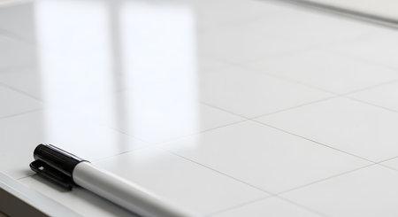 A simple and clean shot of a black dry-erase marker resting on the corner of a blank white magnetic board with faint grid lines. The minimalist composition with ample copy space is ideal for concepts related to business, education, planning, and brainstorming.の素材