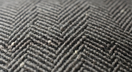 An extreme close-up, macro view of a grey textile with a classic herringbone pattern. The detailed texture of the woven wool or tweed fabric is clearly visible, creating a sophisticated background.の素材