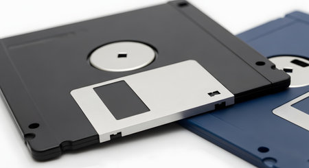 Two vintage 3.5-inch floppy disks, one black and one blue, are placed on a clean white background. This image of obsolete technology evokes nostalgia for early computing and represents old methods of digital data storage.の素材