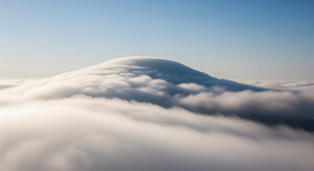 A stunning view of a lenticular cloud formation smoothly capping a mountain peak, which rises above a sea of lower clouds. The scene captures a rare and beautiful meteorological event against a clear blue sky.の素材