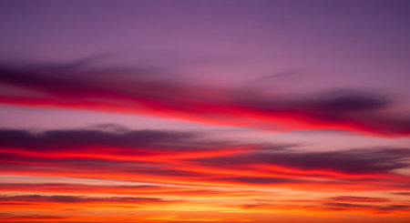 A vertical shot of a dramatic, colorful sky at sunset or twilight. Wispy clouds are illuminated in bright red and magenta hues, set against a deep purple and violet sky. The lower part of the sky still glows with orange.の素材