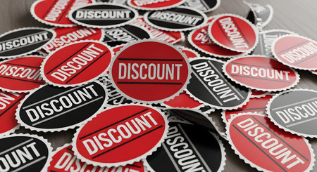 A pile of red, black, and white circular 'DISCOUNT' stickers scattered on a wooden surface. One sticker is prominently featured in the center. This image represents sales, promotions, and retail shopping.の素材