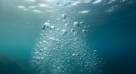 A column of air bubbles rises through deep blue or turquoise water towards the sunlit surface. This underwater scene can represent breathing, scuba diving, life, or simply the abstract beauty of air in water.の素材