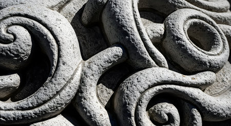 A close-up, detailed macro shot of an intricate, swirling pattern carved into rough, gray stone or granite. The dramatic sunlight creates deep shadows, highlighting the texture and craftsmanship of the ancient-looking relief.の素材