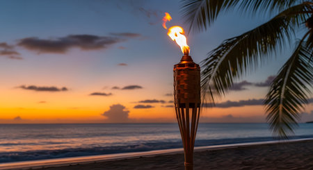 A close-up of a lit tiki torch with a woven bamboo top, its flame burning brightly against a stunning tropical sunset. In the background, the ocean, sandy beach, and the silhouette of a palm frond create a serene, paradise-like atmosphere.の素材