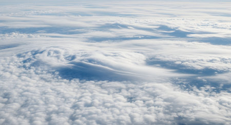 An aerial view from high above the clouds, likely taken from an airplane window. A vast expanse of white, fluffy cumulus and wispy cirrus clouds stretches to the horizon under a pale blue sky. The image conveys a sense of peace, freedom, and travel.の素材