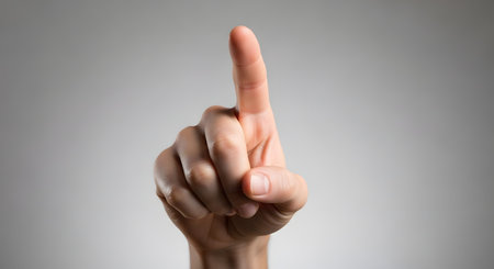 A close-up of a person's hand with the index finger raised and pointing upwards, set against a neutral gray studio background. This gesture can symbolize the number one, having an idea, pointing, or touching a virtual screen.の素材