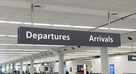 A clear directional sign hangs from the ceiling in a modern airport terminal, indicating the way to 'Departures' and 'Arrivals'. The blurred background shows the spacious interior of the airport, evoking themes of travel, journey, and transportation.の素材