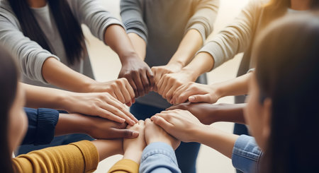 A top-down view of a diverse group of people putting their hands together in a circle. The hands, showing various skin tones, are stacked in the center in a gesture of unity, teamwork, and support. The image conveys concepts of collaboration, community, and shared goals.の素材