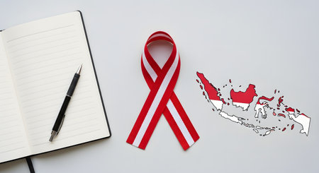 A flat lay composition on a light background featuring a red and white ribbon, an outline map of Indonesia with the national flag, and an open, lined notebook with a pen. This image represents Indonesian patriotism, national planning, or commemorative events.の素材