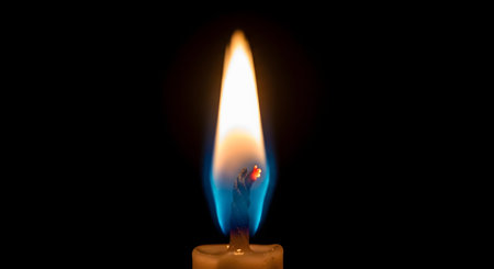 An intimate close-up of a single, steady candle flame glowing brightly against a solid black background. The flame displays a vibrant mix of yellow, orange, and blue colors near the wick, symbolizing hope, peace, and remembrance.の素材
