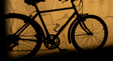 The dark silhouette of a bicycle is cast as a shadow onto a cracked, textured wall illuminated by the warm, yellow-orange light of a setting sun. The image creates a moody, nostalgic, and urban atmosphere. It represents transportation, solitude, and the simple beauty of light and shadow.の素材