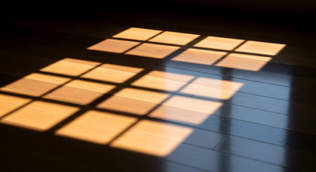 Warm sunlight streams through a window, casting a distinct grid-like shadow of the window panes onto a polished hardwood floor. The interplay of light and shadow creates a peaceful, minimalist, and serene atmosphere in a quiet room.の素材