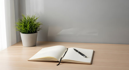 An open, blank notebook and a black pen lie on a clean, light-wood desk. A small potted plant sits to the left, and soft light comes from a window. This minimalist scene represents writing, journaling, planning, or a fresh start.の素材