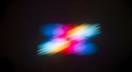 An abstract, colorful light projection on a dark wall. The light is blurred and in motion, creating an 'X' shape with streaks of pink, blue, yellow, and red. This image represents light art, abstract backgrounds, or technology.の素材