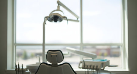 A blurry, out-of-focus shot of a modern dentist's office or exam room. The dental chair is in the foreground, facing a large, bright window. A dental lamp and other equipment are visible but indistinct, creating a soft, sterile, and anonymous feeling.の素材
