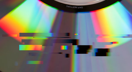 A close-up macro shot of a CD or DVD surface, showing vibrant rainbow holographic reflections. The image is distorted with a digital glitch art effect, featuring pixelated blocks and color bleeding, representing corrupted data or a retro-tech aesthetic.の素材