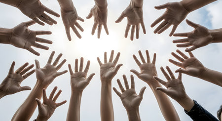 A low-angle view of many diverse hands reaching up towards the sky in a circle, with the sun and clouds in the background. The open hands symbolize unity, community, volunteering, and collective hope or support.の素材