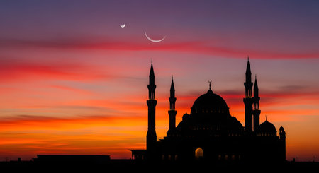 A stunning silhouette of a large mosque with multiple minarets and domes against a vibrant twilight sky. The sky transitions from fiery orange and red near the horizon to deep purple and blue. A large crescent moon and a smaller one shine above the mosque, evoking themes of Ramadan, Eid, or Islamic faith.の素材