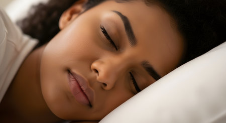 A serene close-up of a beautiful Black woman sleeping peacefully with her head on a white pillow. Her face is relaxed, showcasing her clear skin and natural beauty, conveying rest and tranquility.の素材