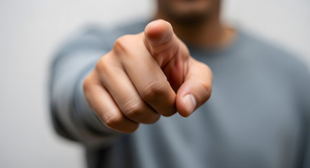 A close-up shot of a man's hand pointing his index finger directly at the camera. The man is wearing a grey shirt and is blurred in the background, with the focus sharply on his hand and finger. The gesture signifies 'you', accusation, or selection.の素材