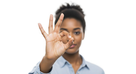 A close-up shot of a Black woman's hand making a perfect "OK" gesture, with her face and blue shirt blurred in the background. The image focuses on the hand sign, symbolizing agreement, approval, or success.の素材