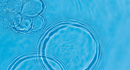 A top-down view of concentric ripples and waves in clear, bright blue water. The patterns are caused by water drops, creating a clean, fresh, and tranquil abstract background for concepts like hydration or purity.の素材