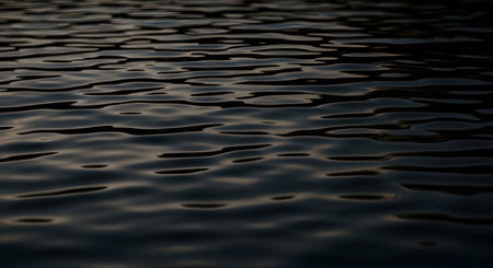 A close-up view of a dark, rippled water surface creating an abstract texture. The gentle waves and low light reflect a moody and mysterious atmosphere, making it an ideal background for nature-themed designs.の素材