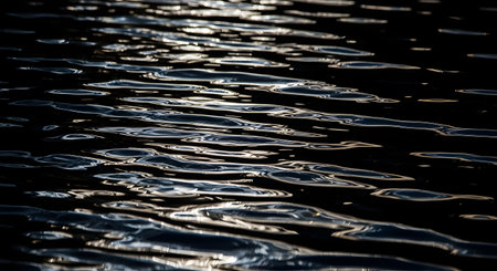 A close-up abstract shot of dark water with small, shimmering ripples reflecting light. The contrast between the dark surface and the bright highlights creates a moody, mysterious, and tranquil texture.の素材