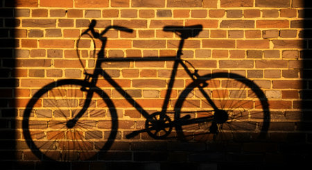 The shadow of a bicycle cast onto a red brick wall during the golden hour. The low-angle sun creates a clear, dark silhouette of the bike, highlighting its frame, wheels, and handlebars.の素材