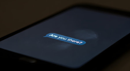 A close-up macro shot of a smartphone screen in the dark, displaying a single, glowing blue text message bubble that says 'Are you there?'. The message evokes feelings of loneliness, waiting, or concern.の素材