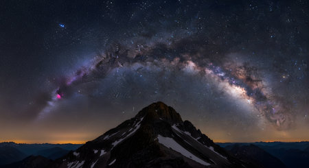 A stunning astrophotography shot of the Milky Way galaxy arching across the night sky. The vibrant core and colorful nebulas are visible above a majestic, snow-capped mountain peak.の素材
