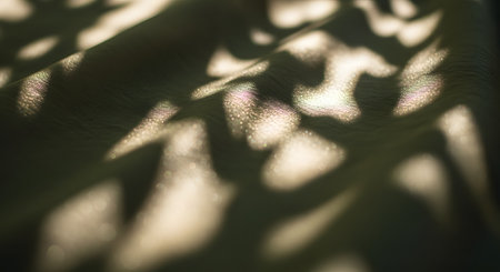 Abstract patterns of dappled sunlight and shadows dance across a textured green fabric surface. The interplay of light and dark creates a soft, organic design reminiscent of leaves filtering sun, suitable for backgrounds.の素材
