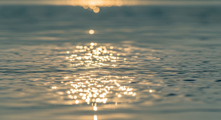 Golden sunlight reflects off the gentle ripples of a water surface, creating a sparkling bokeh effect. The abstract nature shot captures the serene and shimmering beauty of a lake or ocean at sunset.の素材