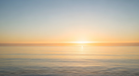 A serene and minimalist view of a calm ocean at sunset, with the horizon line clearly dividing the golden sky and the gentle water. The warm light creates a peaceful and meditative atmosphere.の素材