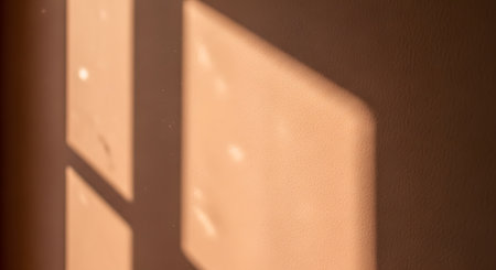 Abstract geometric shadows cast by a window frame onto a textured peach-colored wall, illuminated by warm sunlight. Floating dust particles add atmosphere to the minimalist interior scene.の素材