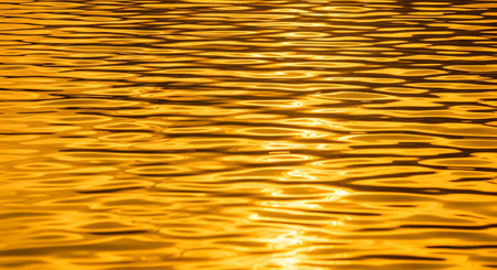 The surface of the water is bathed in golden light, creating a mesmerizing pattern of ripples and waves. The high-contrast, abstract texture reflects the warmth of a sunset or sunrise, evoking feelings of calm and wealth.の素材