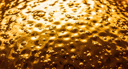 A macro view of a golden liquid surface filled with bubbles and ripples, resembling oil or molten gold. The glossy, textured appearance creates a rich and abstract background.の素材