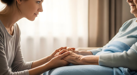 A close-up heartwarming image of a younger woman holding the wrinkled hands of an elderly woman. The gesture conveys compassion, care, love, and support, typical of a caregiver or family member comforting a senior.の素材