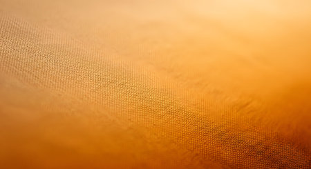 A macro close-up view of a textured orange fabric surface, highlighting the woven cross-hatch pattern. The warm color and soft lighting gradient make it an ideal abstract background for design projects.の素材