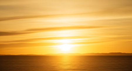 A breathtaking golden sunset illuminates the horizon over a calm, vast ocean. The soft, horizontal clouds and the reflection on the water create a peaceful and minimalist seascape.の素材