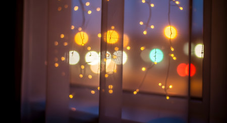 Warm, colorful city lights bokeh shining through sheer white curtains and window blinds at night. The soft, defocused aesthetic creates a cozy, dreamy, and urban evening atmosphere.の素材