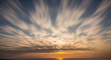 A long exposure photograph captures clouds moving rapidly outwards from the center of the sky during sunset, creating a dynamic zoom burst effect. The motion blur streaks are illuminated by warm orange light.の素材