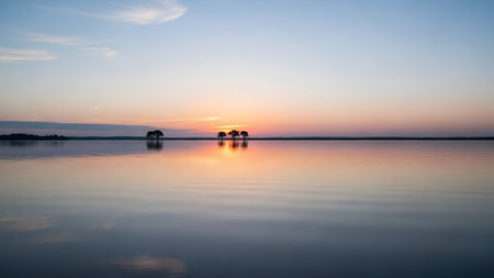 A minimalist landscape featuring a row of silhouette trees standing in the center of a calm lake at sunset. The pastel gradient sky reflects perfectly on the smooth water creating a symmetrical and tranquil atmosphere.の素材