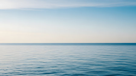 A minimalist landscape features a perfectly calm, clear blue ocean with gentle ripples extending to a subtle horizon line against a pale blue and white sky. The composition conveys tranquility, vastness, and a serene natural environment.の素材